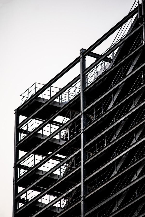 A black and white image of a steel structure framework of a building under construction. The expertly crafted steel design, featuring a skeletal frame with multiple floors and staircases, is exposed against the backdrop of a clear sky.