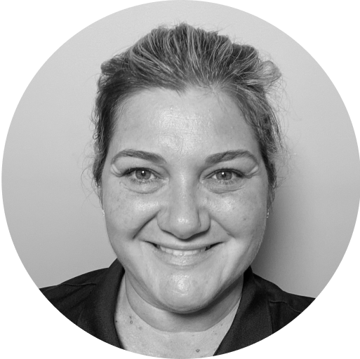 Black and white close-up portrait of a person with light-colored hair pulled back. They are smiling and wearing a collared shirt. The background is plain and light-colored.