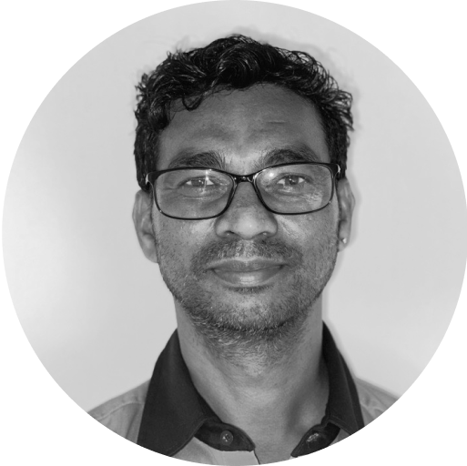 A black-and-white portrait of a man wearing glasses, a collared shirt, and a slight smile. The background is plain, and the image is cropped in a circular frame.