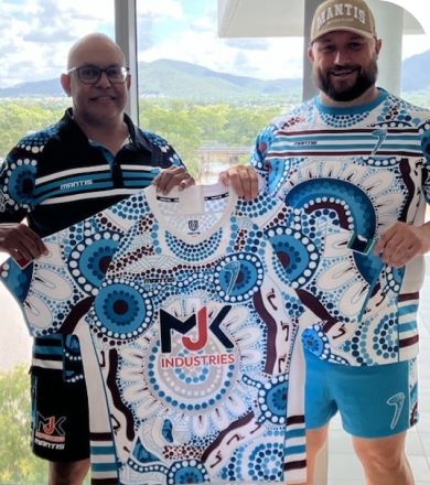 Two men smile while holding an intricately designed sports jersey between them. The jersey features a vibrant, symmetrical pattern in blue, white, and brown with the NJK Industries logo prominently displayed in the center. They both wear matching outfits.